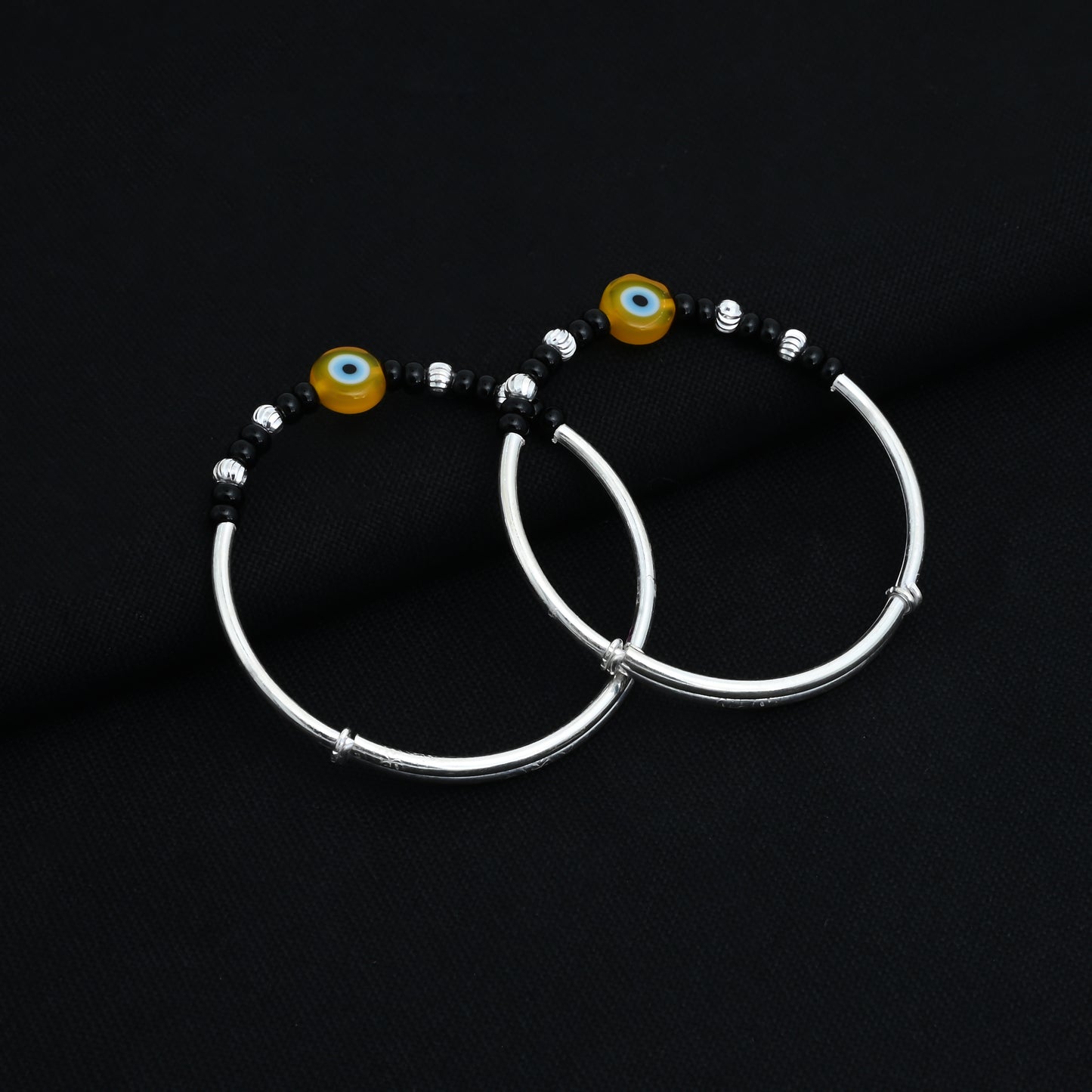 Silver baby kada payal with a protective yellow evil eye design and black and silver bead accents.