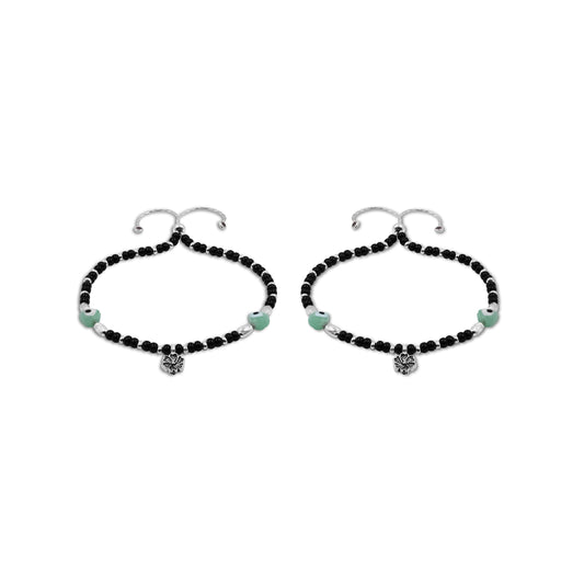 Elegant silver anklet with black beads, an evil eye charm, and delicate floral details, offering a fashionable touch.