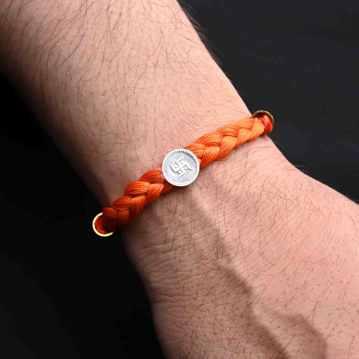 Elegant Rakhi with a silver Swastika and bold orange tangle Moli, ideal for boys.
