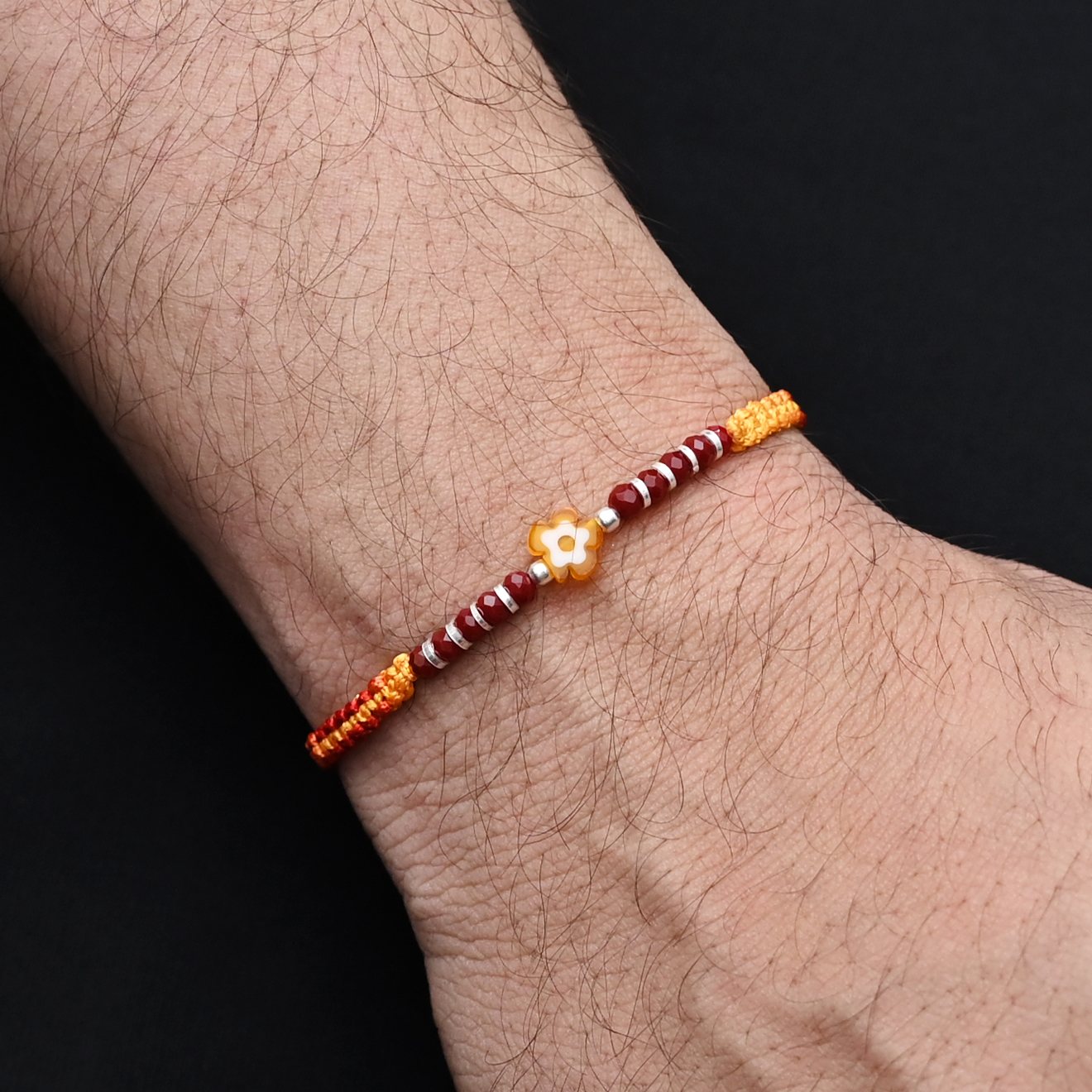 Elegant Rakhi with a silver yellow flower centerpiece and silver and light red beads, ideal for boys.