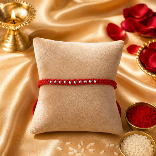 925 Silver Bead Rakhi with handcrafted red thread displayed on a beige velvet cushion with diya, kumkum, rice, and festive Raksha Bandhan decorations.