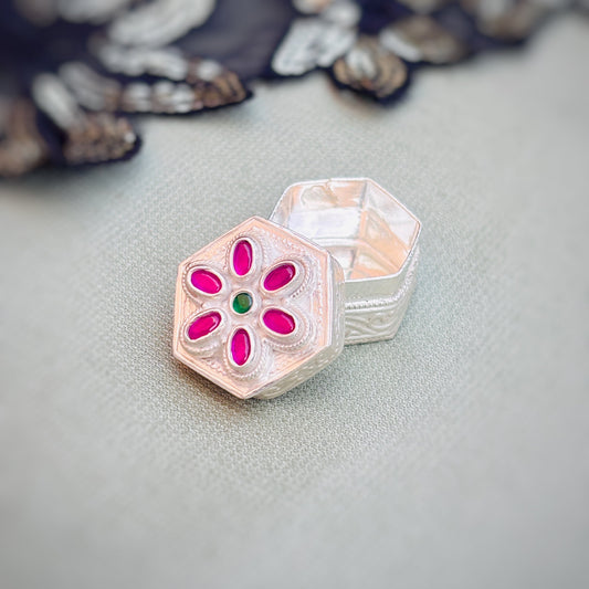 Elegant silver sindor box featuring pink stones and a green center stone in a flower design.