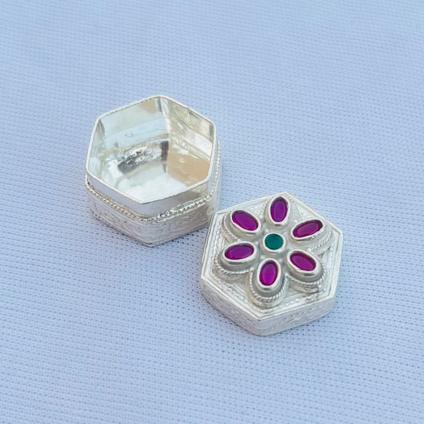 Silver sindor box with pink stones and a green center stone in an intricate flower motif.