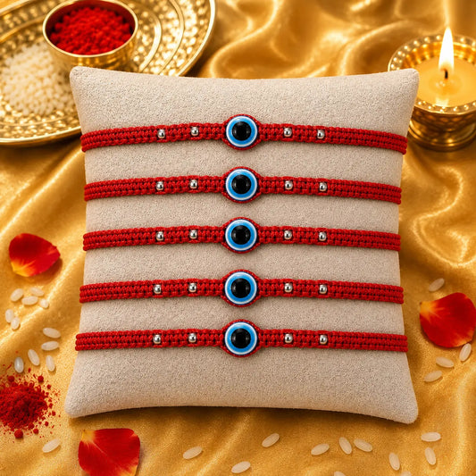 Premium evil eye rakhi with red thread placed on cushion with golden festive background, diya and kumkum for Raksha Bandhan