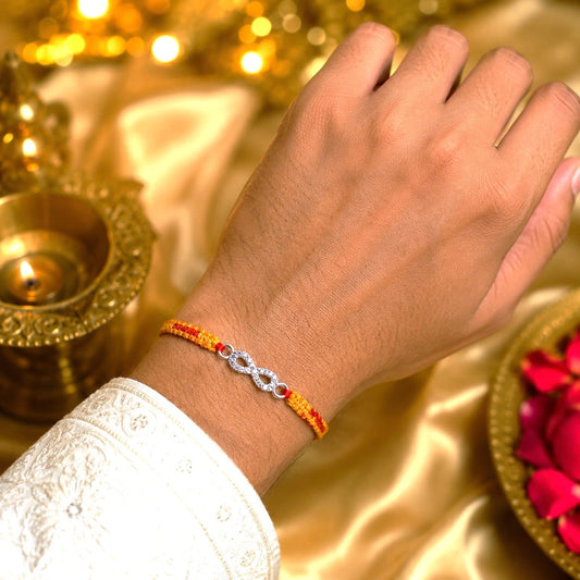 Silver Infinity BRO Rakhi for brother with sparkling infinity charm and orange-red handcrafted thread displayed on a beige velvet cushion