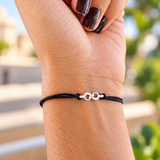 Silver infinity bracelet with black thread worn on wrist