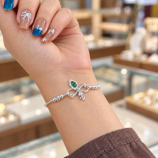 Silver bracelet with colorful peacock feather eye, Trishul and sun charms worn on a woman's wrist