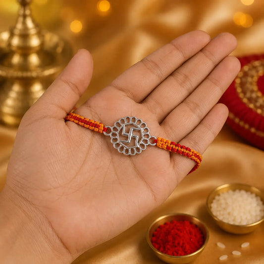 925 Sterling Silver Swastik Rakhi displayed on a premium beige cushion with festive Raksha Bandhan decor including kumkum, rice, marigold flowers, brass pooja thali, and diya.