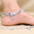 Delicate silver anklet adorned with floral motifs and gemstones.