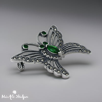 Elegant silver saree pin featuring a butterfly design embellished with green stones for a stylish look.