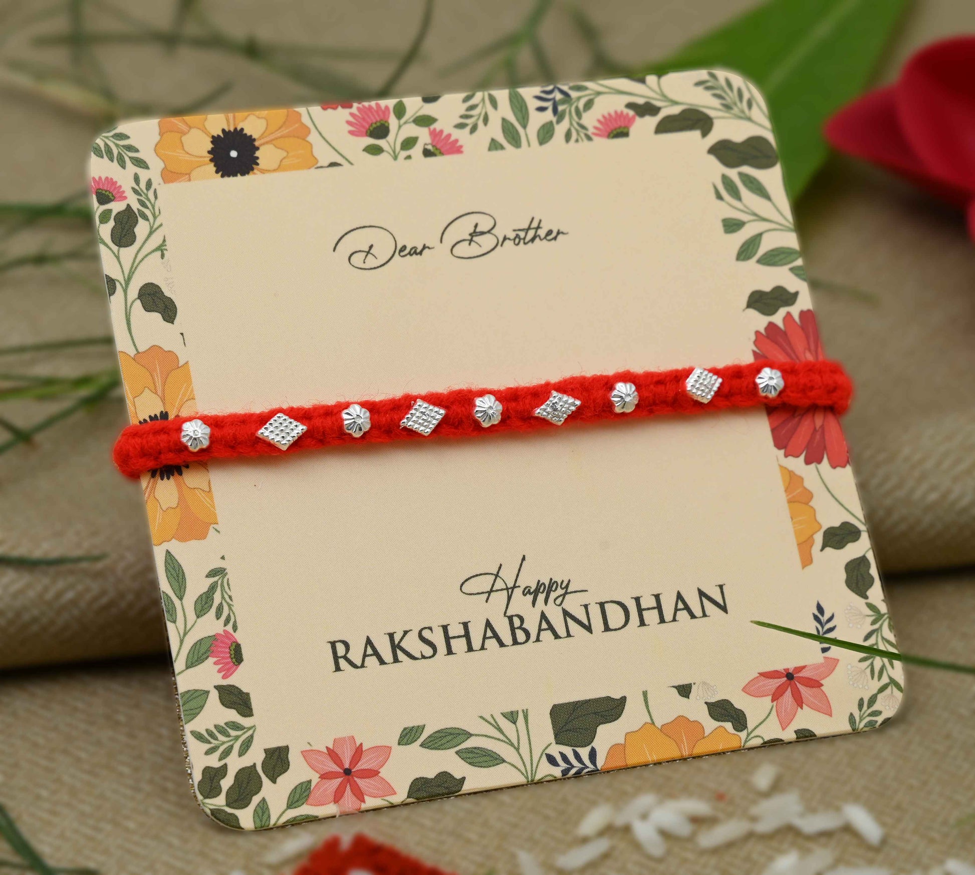 Silver Rakhi with a small flower design and vibrant orange thread, perfect for boys