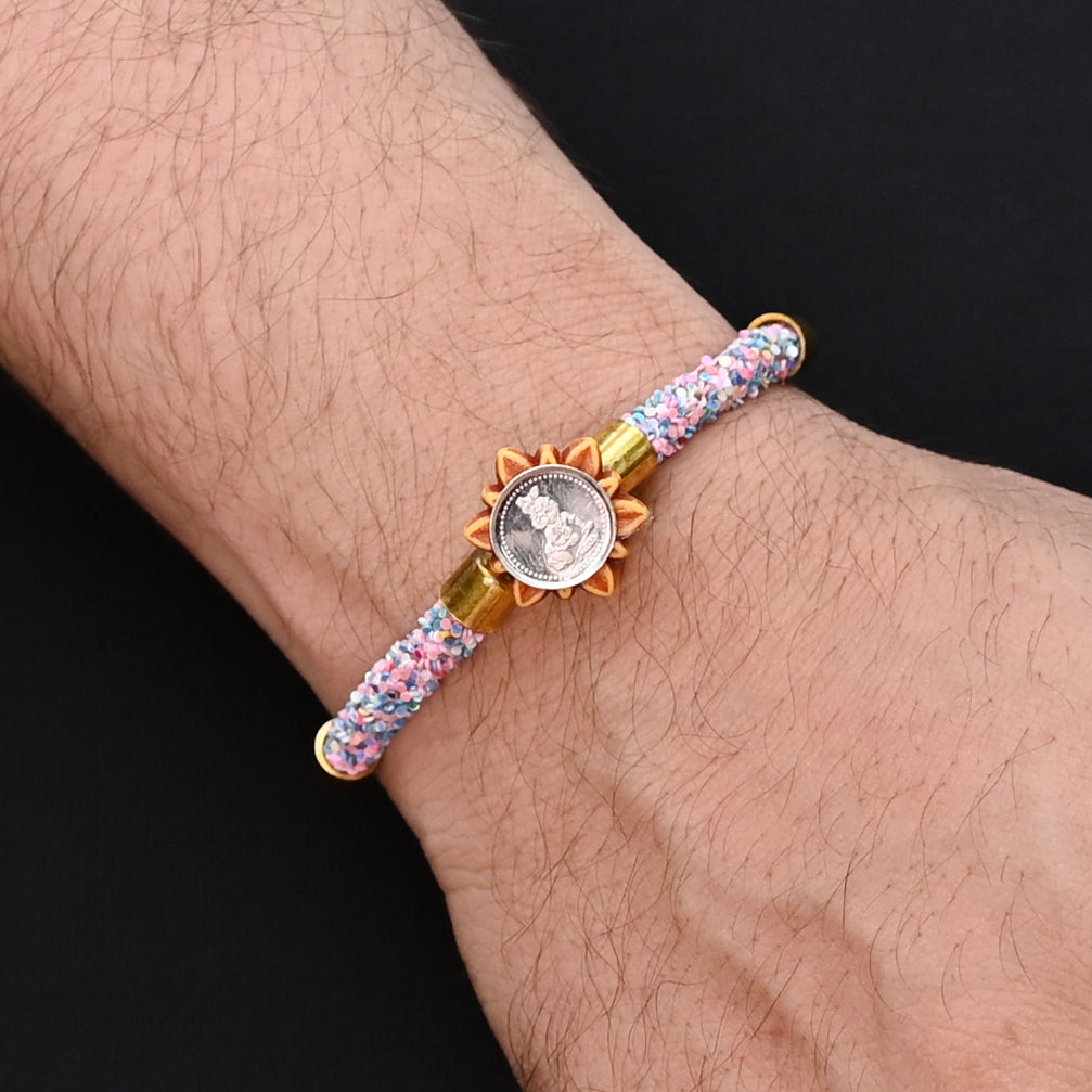 Traditional Rakhi for boys with silver Baal Gopal and colorful pink and blue plastic beads.