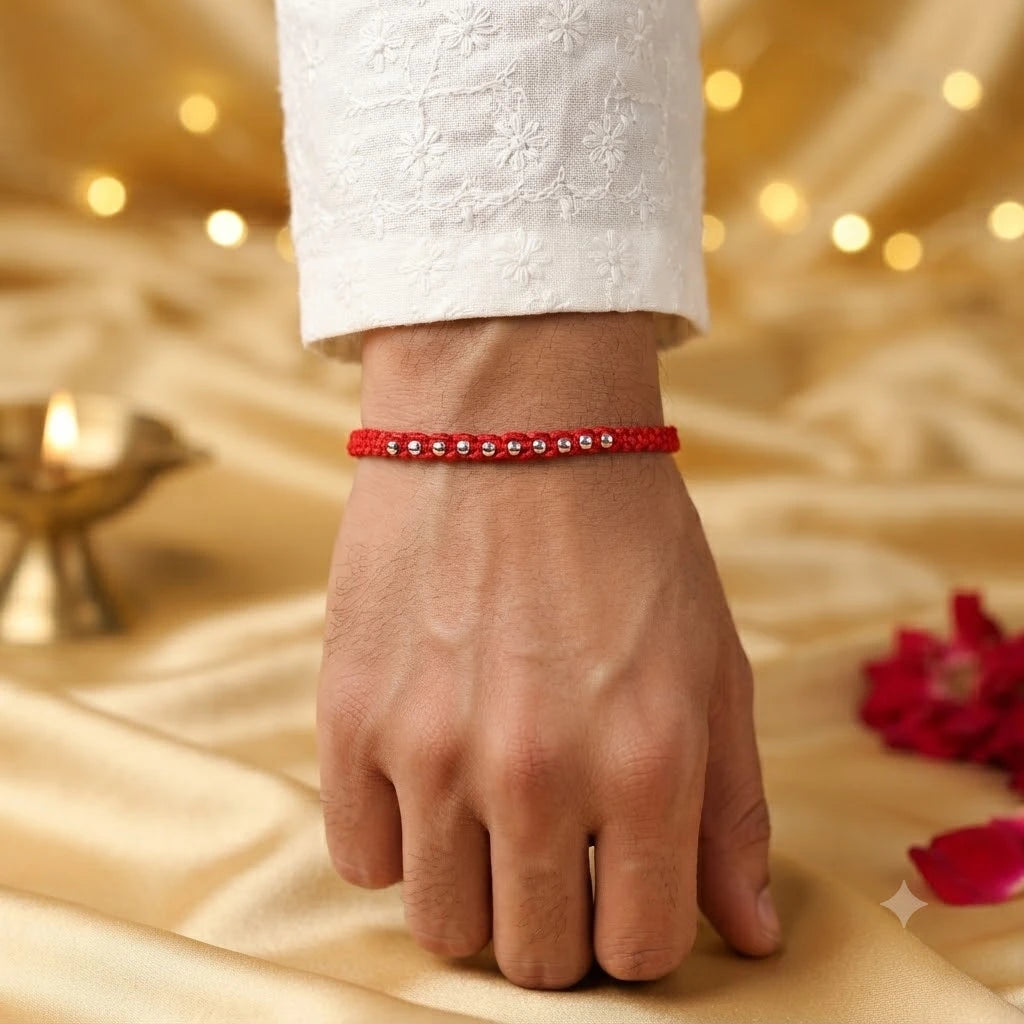 925 Silver Bead Rakhi with handcrafted red thread displayed on a beige velvet cushion with diya, kumkum, rice, and festive Raksha Bandhan decorations.