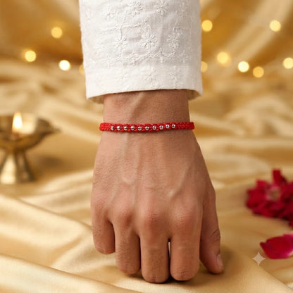 925 Silver Bead Rakhi with handcrafted red thread displayed on a beige velvet cushion with diya, kumkum, rice, and festive Raksha Bandhan decorations.