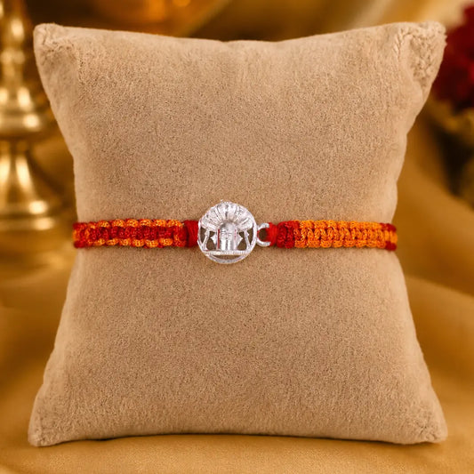 925 Sterling Silver Shivling Rakhi with traditional red and orange braided thread for Raksha Bandhan displayed on a premium beige velvet cushion.