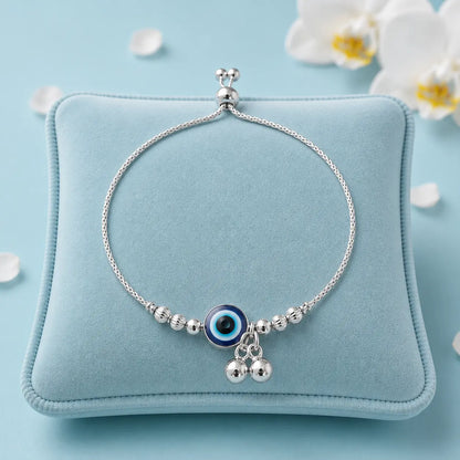 925 Sterling Silver Evil Eye Adjustable Bracelet displayed on a soft blue velvet jewelry cushion with white orchid flowers and luxury studio lighting.