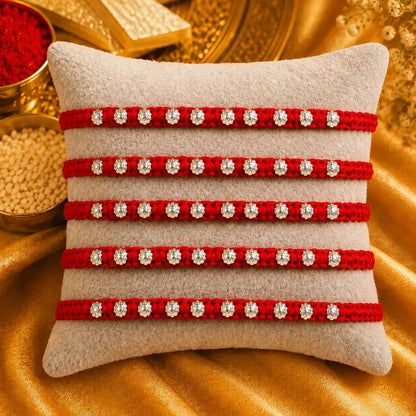 Red Rakhi with silver beads displayed on a beige cushion with golden festive background