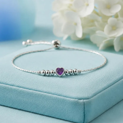 925 sterling silver adjustable bracelet with a purple heart-shaped gemstone, silver beads, and sliding clasp displayed on a light blue velvet jewelry box.