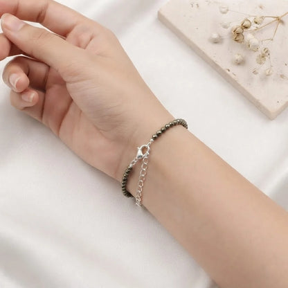 Natural faceted pyrite beaded bracelet with a silver clasp resting on minimalist white display blocks.