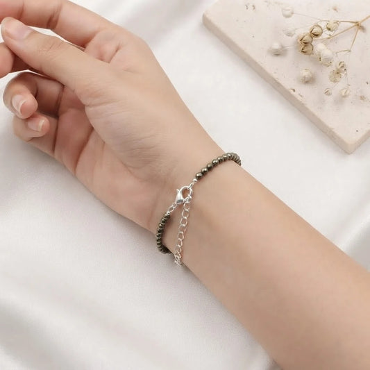 Natural faceted pyrite beaded bracelet with a silver clasp resting on minimalist white display blocks.