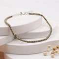 Natural faceted pyrite beaded bracelet with a silver clasp resting on minimalist white display blocks.