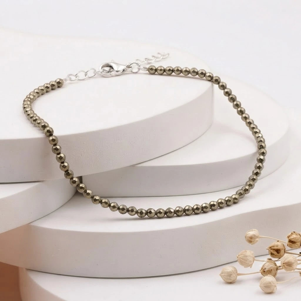 Natural faceted pyrite beaded bracelet with a silver clasp resting on minimalist white display blocks.