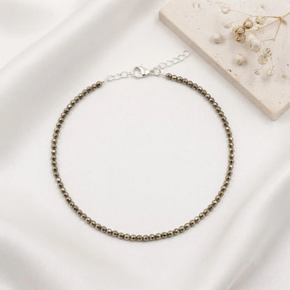 Natural faceted pyrite beaded bracelet with a silver clasp resting on minimalist white display blocks.