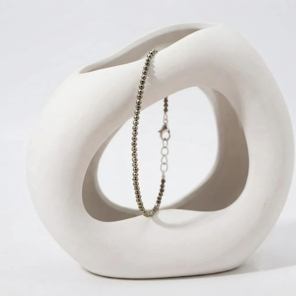 Natural faceted pyrite beaded bracelet with a silver clasp resting on minimalist white display blocks.