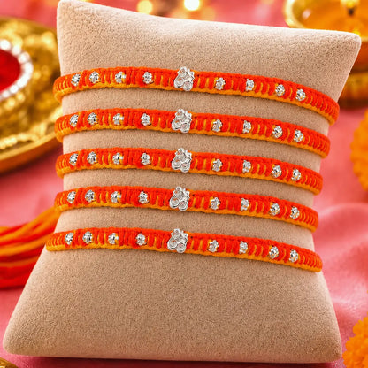 Set of five orange and yellow thread designer silver rakhis displayed on a beige cushion