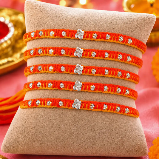 Set of five orange and yellow thread designer silver rakhis displayed on a beige cushion