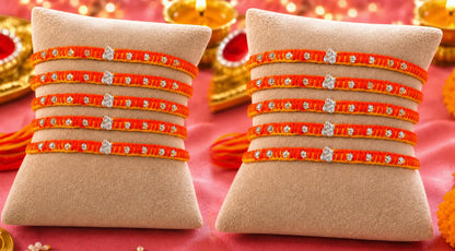 Set of 10 orange and yellow thread designer silver rakhis displayed on a beige cushion