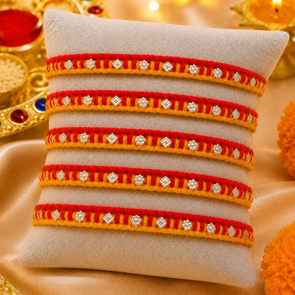Traditional red and yellow Rakhi with silver detailing displayed on a cream velvet cushion