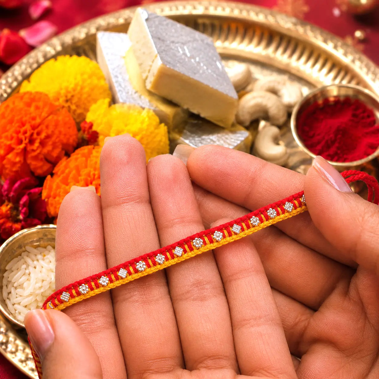 Traditional red and yellow Rakhi with silver detailing displayed on a cream velvet cushion