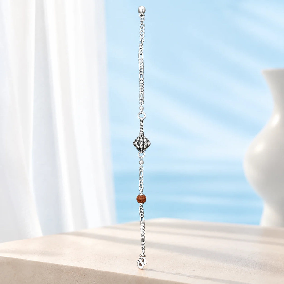 Hanuman Ji Ki Ghota silver bracelet with decorative silver chain and brown Rudraksha-style bead on a brown jewellery display