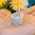 Handcrafted silver sindor box with pink stones and green center stone in flower motif.