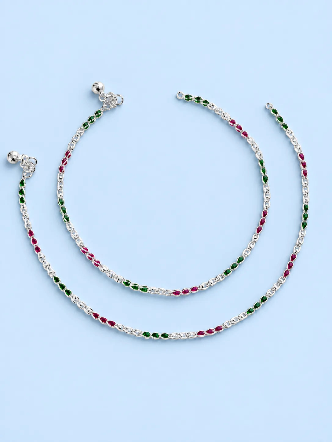 A pair of silver chain anklets with alternating green and red oval beads, displayed on a light blue background.