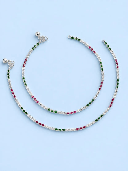A pair of silver chain anklets with alternating green and red oval beads, displayed on a light blue background.