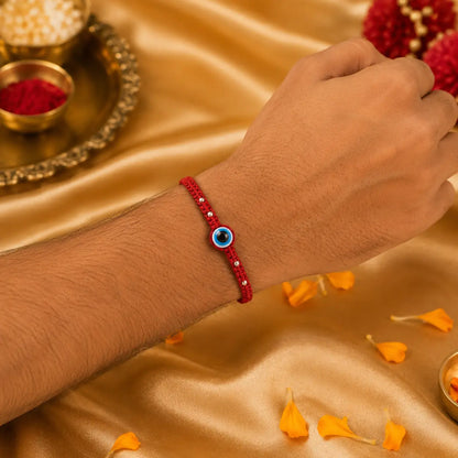 Premium evil eye rakhi with red thread placed on cushion with golden festive background, diya and kumkum for Raksha Bandhan