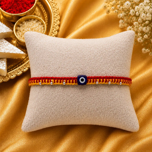 Premium handmade Evil Eye Rakhi with blue protective bead on a cream cushion, luxury golden festive background with kumkum, rice, sweets, and flowers for Raksha Bandhan.