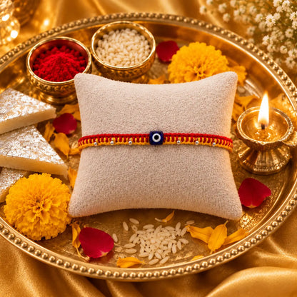 Premium handmade Evil Eye Rakhi with blue protective bead on a cream cushion, luxury golden festive background with kumkum, rice, sweets, and flowers for Raksha Bandhan.