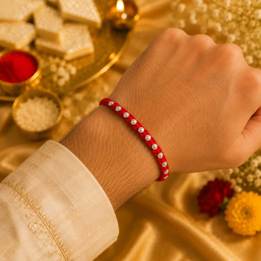 Red Rakhi with silver beads displayed on a beige cushion with golden festive background