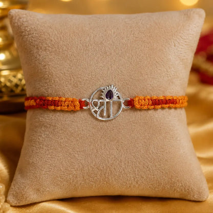 Shree silver rakhi with purple stone and red orange thread on golden satin background