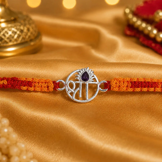 Shree silver rakhi with purple stone and red orange thread on golden satin background