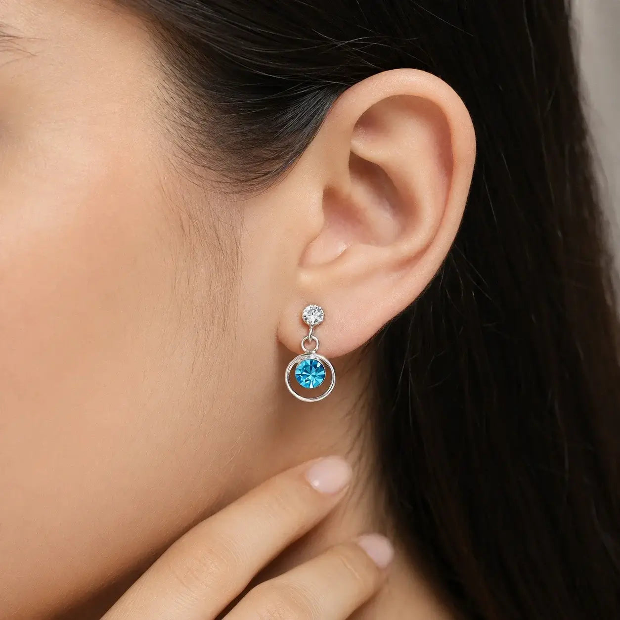 Silver blue round cubic zirconia open circle drop earrings for women with polished silver finish and sparkling crystal accents displayed on a white rose branch.