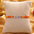 Silver Infinity BRO Rakhi for brother with sparkling infinity charm and orange-red handcrafted thread displayed on a beige velvet cushion