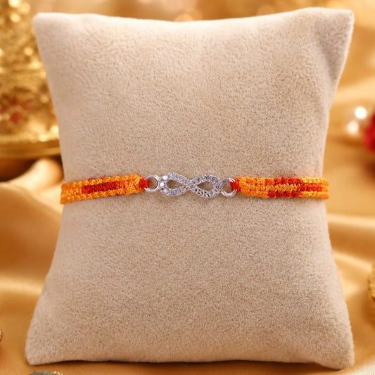 Silver Infinity BRO Rakhi for brother with sparkling infinity charm and orange-red handcrafted thread displayed on a beige velvet cushion