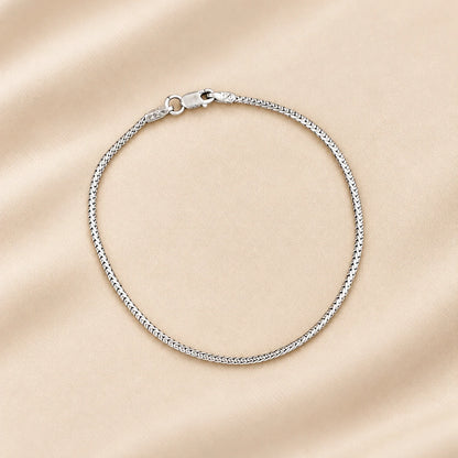 A silver chain bracelet with a textured, rope-like link design and a lobster clasp, displayed on a soft beige satin fabric background.