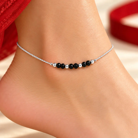 Silver anklet pair with black beads on a beige background by Khushbu Jewellers