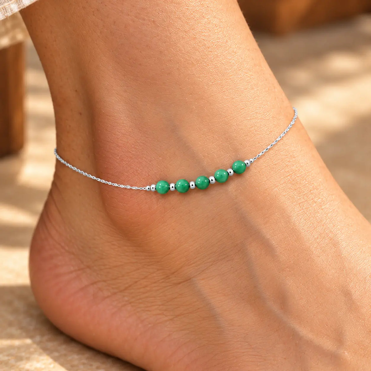 Silver anklet with green beads worn on a woman's ankle by Khushbu Jewellers