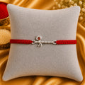 Silver Basuri Rakhi with red mauli thread on a white cushion with golden festive background